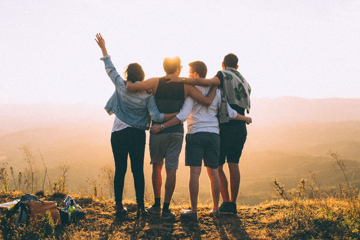 Un gruppo di giovani amici abbracciati al tramonto in montagna