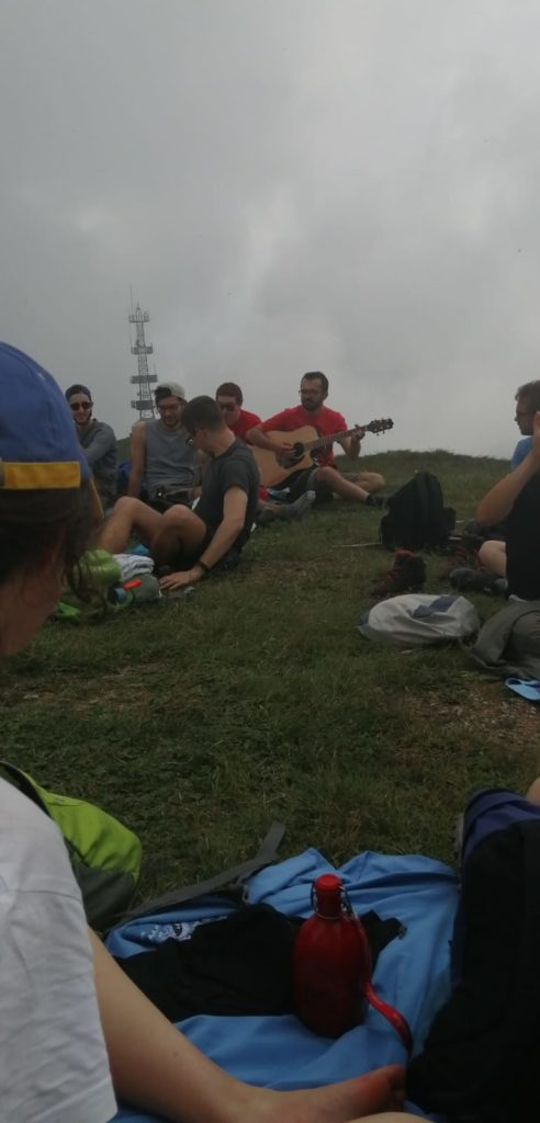 Un gruppo di amici canta con la chitarra seduto sul prato in vetta