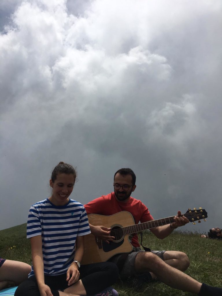 Due ragazzi cantano e suonano la chitarra sul prato in montagna